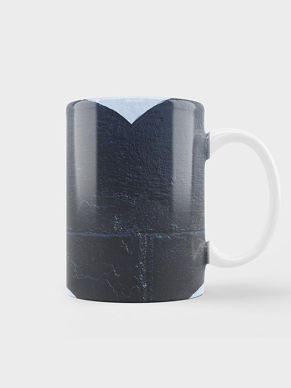 Taza de cerámica blanca con un diseño azul oscuro texturizado en forma de corazón en su superficie, colocado sobre un fondo liso gris claro.