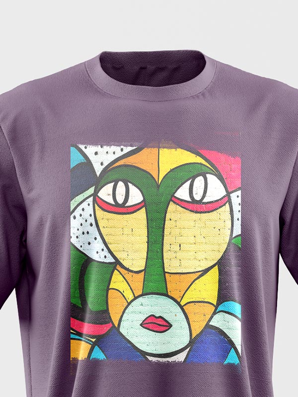 Camiseta morada con un colorido diseño de cara abstracta de estilo cubista, con grandes ojos, labios rojos y formas geométricas en verde, amarillo, azul, rojo y blanco.