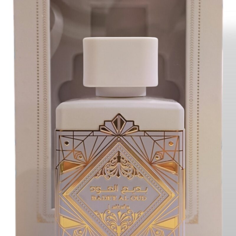 Un frasco de perfume blanco con diseños geométricos dorados y texto en árabe, etiquetado Lattafa Asad Zanzibar EDP 100ml, se muestra delante de su caja abierta a juego con decoraciones ornamentales.