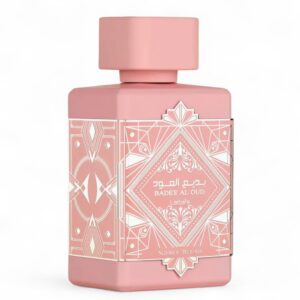 El frasco de perfume Lattafa Badee Al Oud Noble Blush EDP 100 ml, de color rosa, presenta motivos geométricos dorados y texto en árabe, con el nombre de la fragancia Noble Blush en la parte inferior.