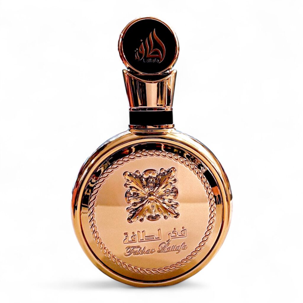 Un frasco redondo de perfume dorado con la etiqueta Lattafa Fakhar Gold Extrait EDP 100ml, con escritura árabe grabada, detalles ornamentales, un tapón decorativo y un diseño central inspirado en una mariposa.