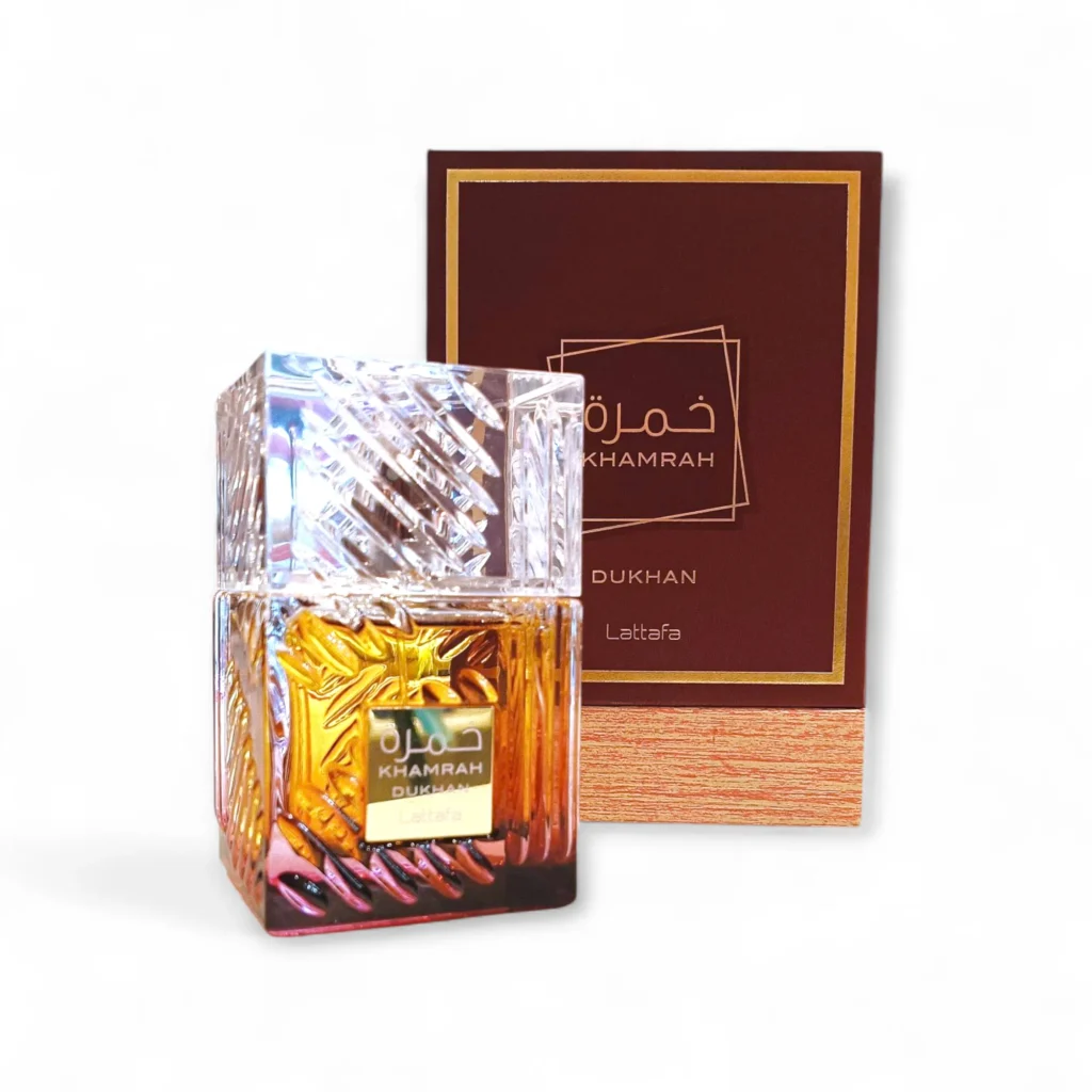 Un frasco de perfume cuadrado de cristal texturizado, con la etiqueta Khamrah de Lattafa, se coloca delante de una caja marrón y dorada a juego con texto en árabe e inglés.