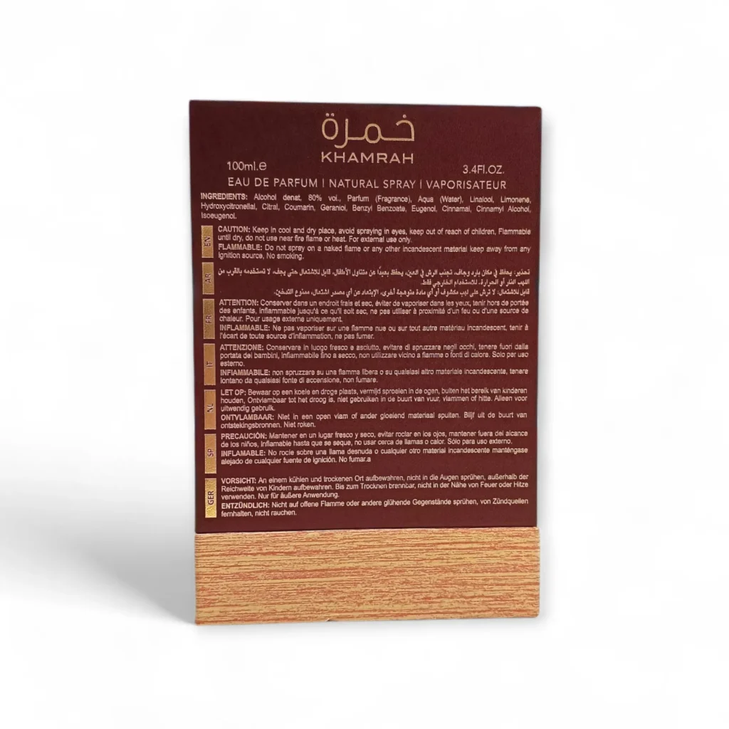 Reverso de una caja de perfume Khamrah, con detalles del producto, ingredientes, advertencias, instrucciones e información del fabricante en inglés y francés, con fondo granate y diseño de vetas de madera en la parte inferior.