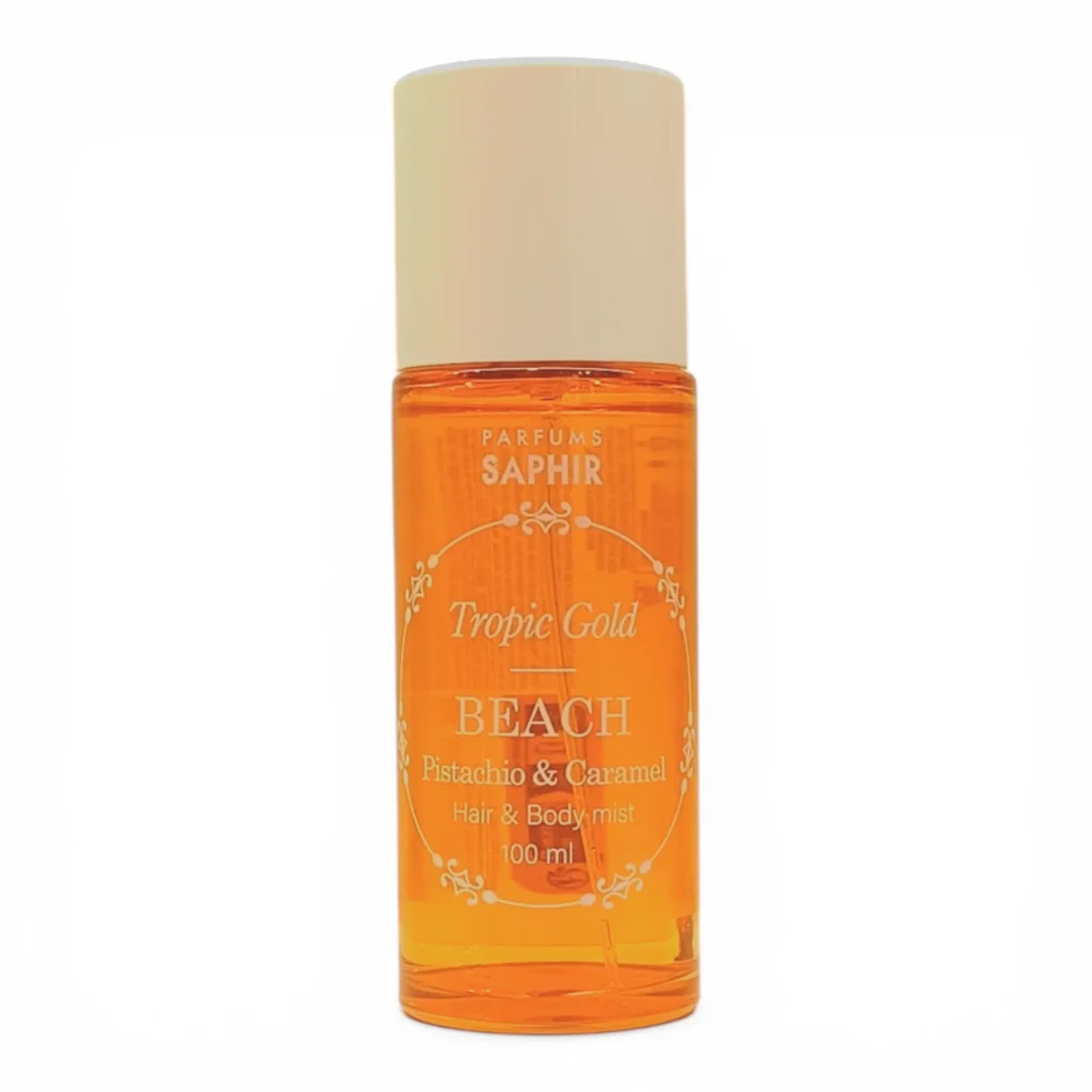 Un frasco de 100 ml de Parfums Saphir Tropic Gold BEACH Pistachio & Caramel Hair & Body Mist con un líquido ámbar anaranjado y un tapón beige, fotografiado sobre un fondo blanco.