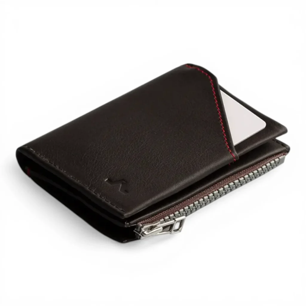 Una cartera de piel negra con cremallera plateada y pespuntes rojos, con una tarjeta visible parcialmente insertada en una ranura exterior.