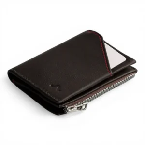 Una cartera de piel negra con cremallera plateada y pespuntes rojos, con una tarjeta visible parcialmente insertada en una ranura exterior.