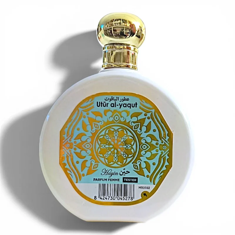 Frasco redondo de perfume blanco con tapón dorado y etiqueta decorativa dorada en la que se lee Utur al-yaqut en árabe e inglés, con Hajun Parfum Femme Tester debajo de un motivo floral. Frasco redondo de perfume blanco con tapón dorado y etiqueta decorativa dorada en la que se lee Utur al-yaqut en árabe e inglés, con Hajun Parfum Femme Tester debajo de un motivo floral.