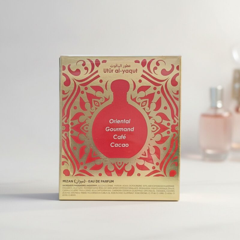 Caja de perfume dorada y roja etiquetada como Utúr al-yaqut con motivos decorativos y las notas olfativas Oriental Gourmand, Café, Cacao. En el fondo se ven frascos de perfume difuminados. Caja de perfume dorada y roja etiquetada como Utúr al-yaqut con motivos decorativos y las notas olfativas Oriental Gourmand, Café, Cacao. En el fondo se ven frascos de perfume difuminados.